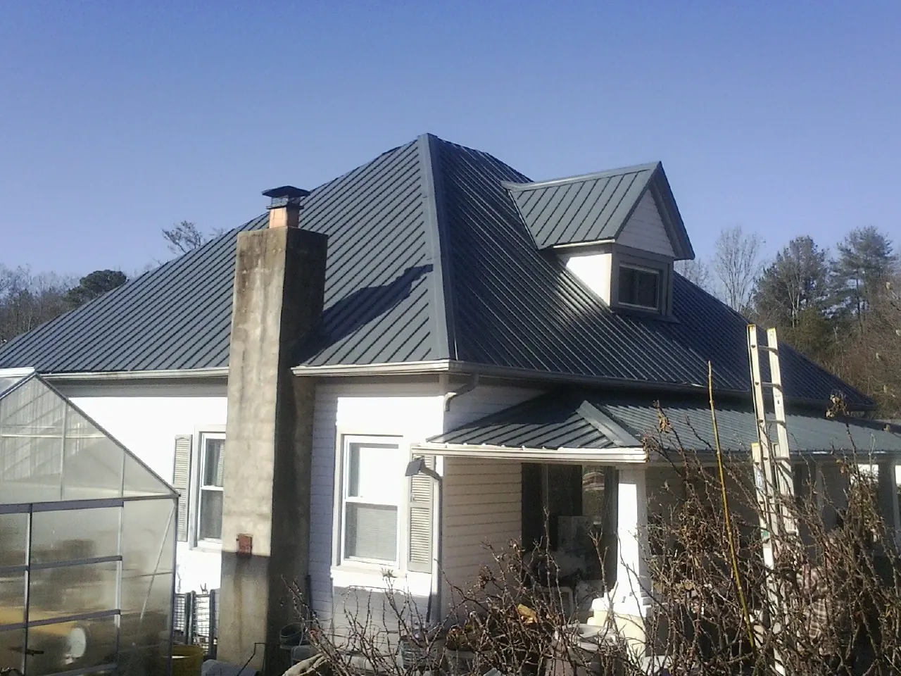 Dark blue standing seam metal roof on a white farmhouse with dormer — Slate & Tile Roof Repair by Roofing Brothers in Burns