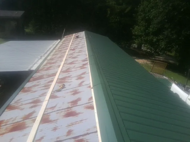 Old rusted panels beside newly installed green metal roofing — Wind Damage Roof Repair by Roofing Brothers in Burns