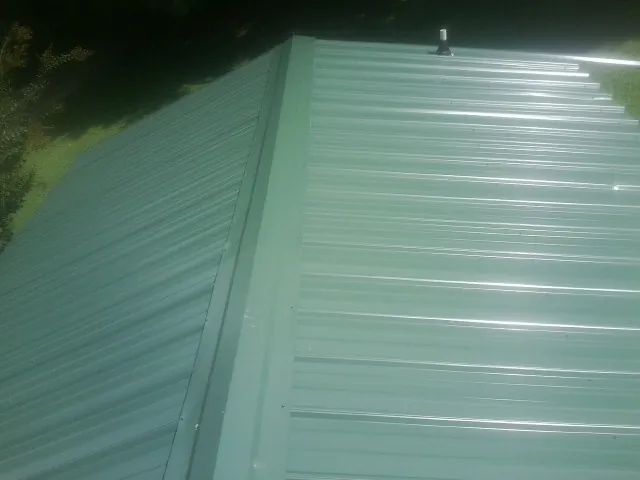 New green metal panels meeting at the ridge of a roof — Flat Roof Repair work by our crew in Burns