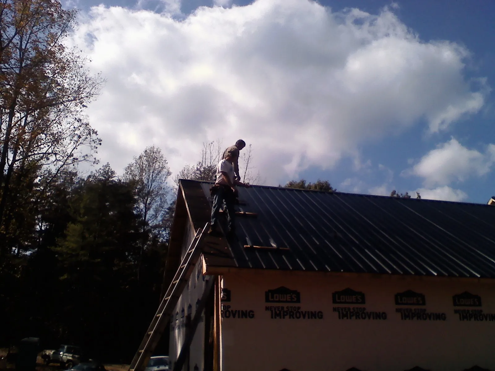 Roofer fastening dark metal panels high against a cloudy sky, from a Roof Inspection job in Burns
